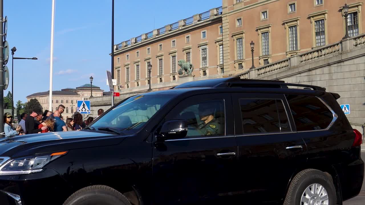Black SUV driving past the Royal Palace in Stockholm with a crowd gathered