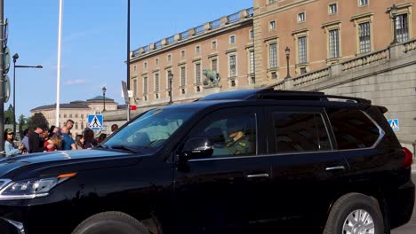 black suv driving past the royal palace in stockholm with a crowd gathered
