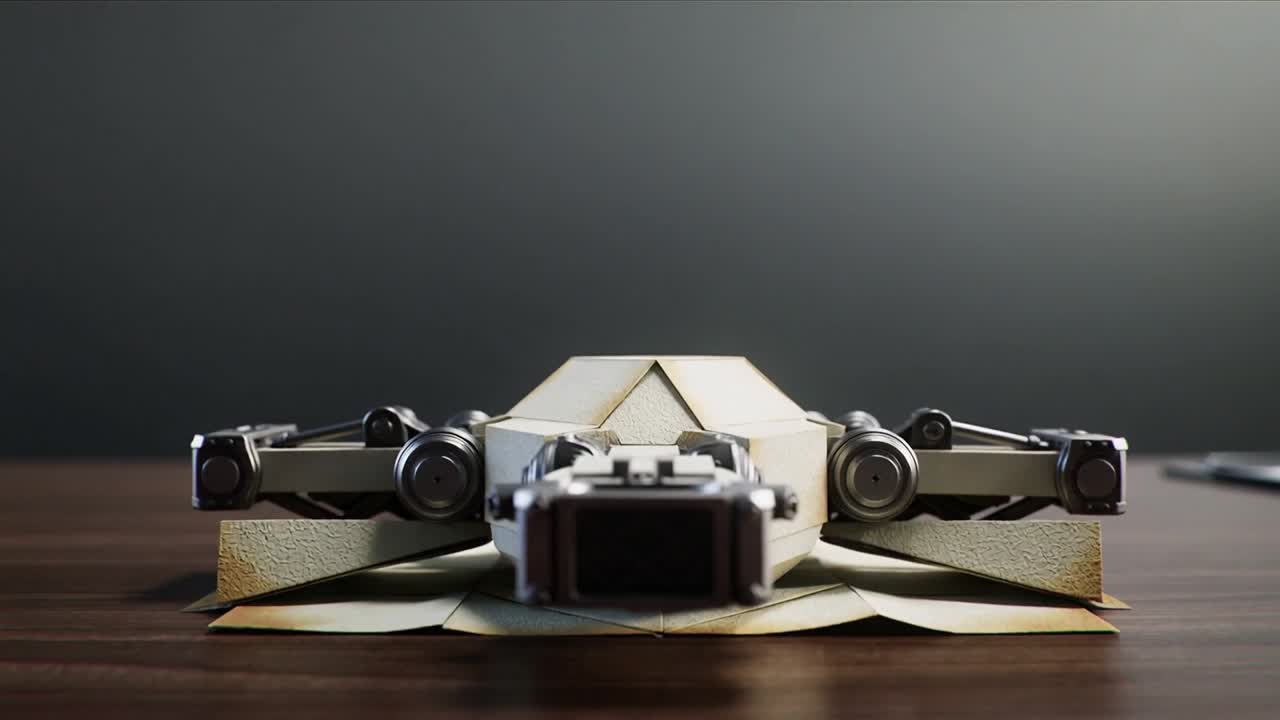 Drone kertas lipat sedang terbentang, mengaktifkan engsel, memperlihatkan lengan logam di atas meja kayu, siap untuk terbang.