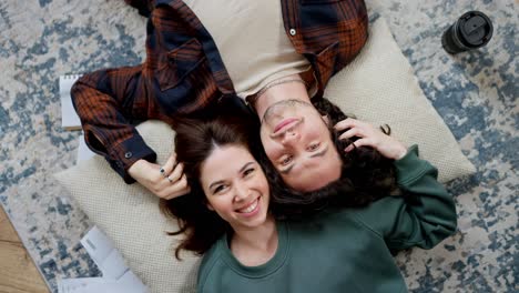 top view rotating camera happy brunette girl holding and touching hair of her boyfriend with curly hair lying on pillow head to head on floor in modern apartment at home