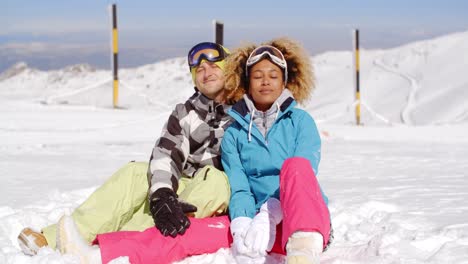 Couple-sitting-in-snow-on-ski-slope