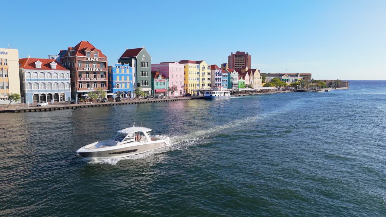 Aerial pullback of Punda District’s colorful waterfront buildings with a boat passing in Willemstad, Curacao