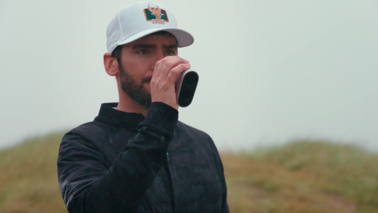 close up seguimiento tiro de golfista masculino elevando el buscador de rango a los ojos en cámara lenta mientras lee yardage para fijar desde el fairway para el enfoque tiro en el campo de golf de ireland links