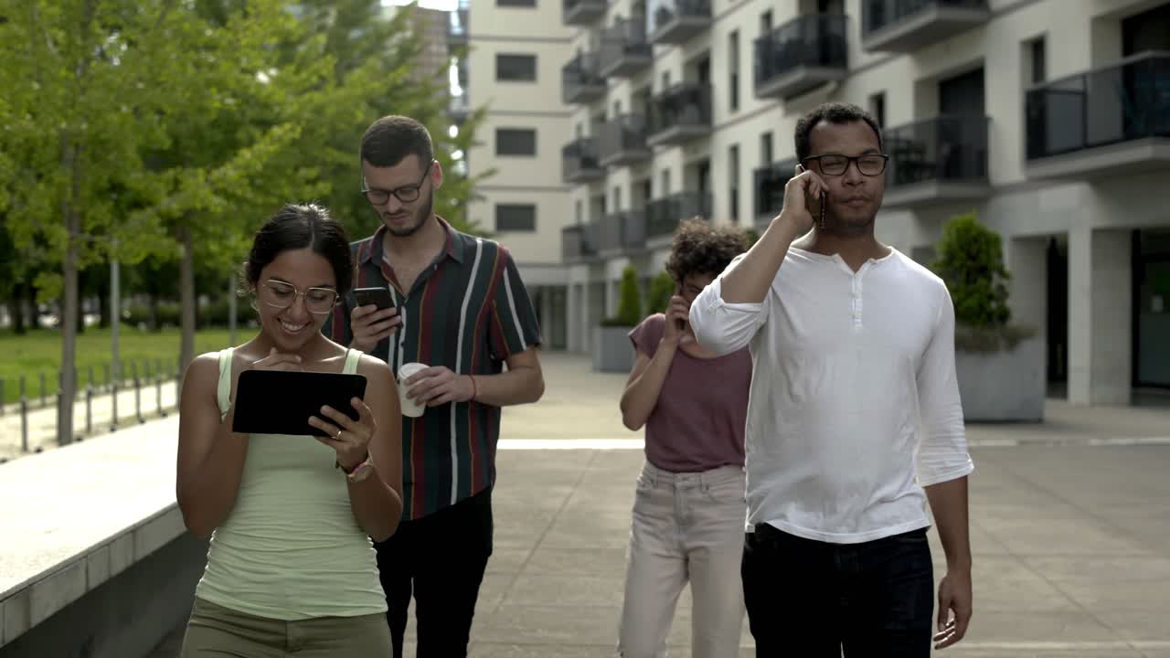 jóvenes sonrientes con dispositivos digitales paseando por la calle.