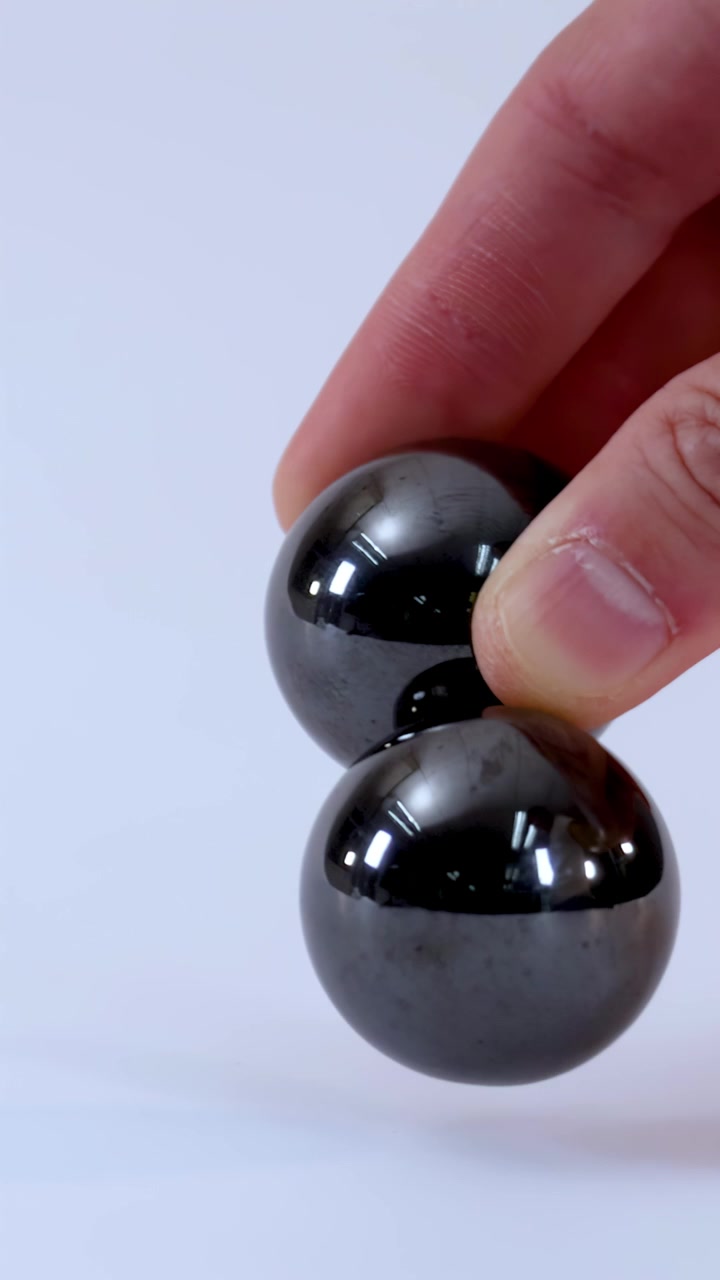 A hand holds and manipulates two metallic magnetic balls against a clean white studio background