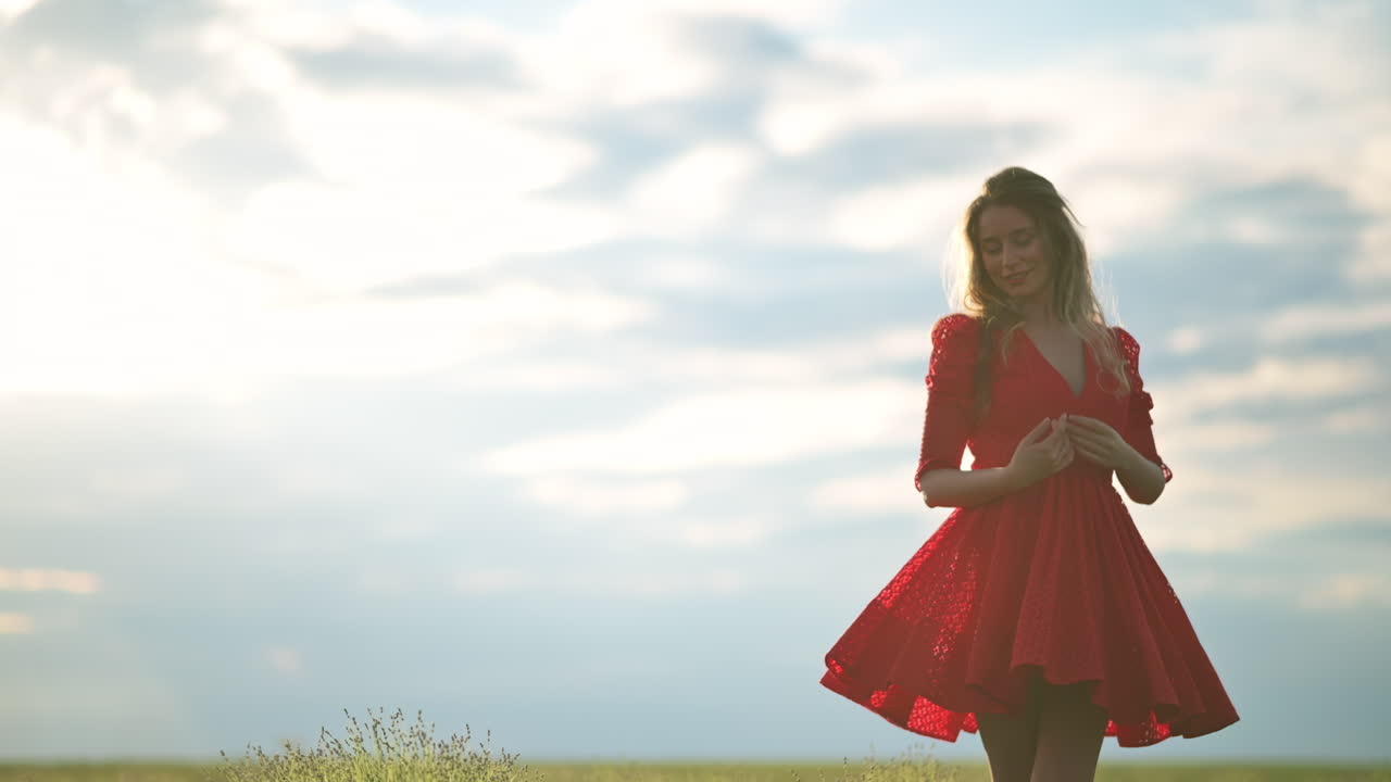 A woman in a red dress stands in a wide green field, lifting her arms toward the sky in a moment of gratitude and joy
