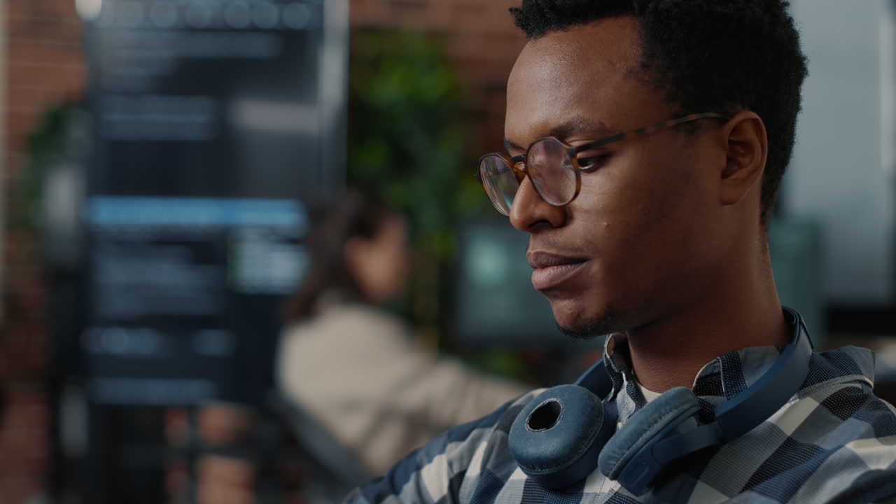 Closeup portrait of software engineer writing code fixing glasses and smiling sitting at desk