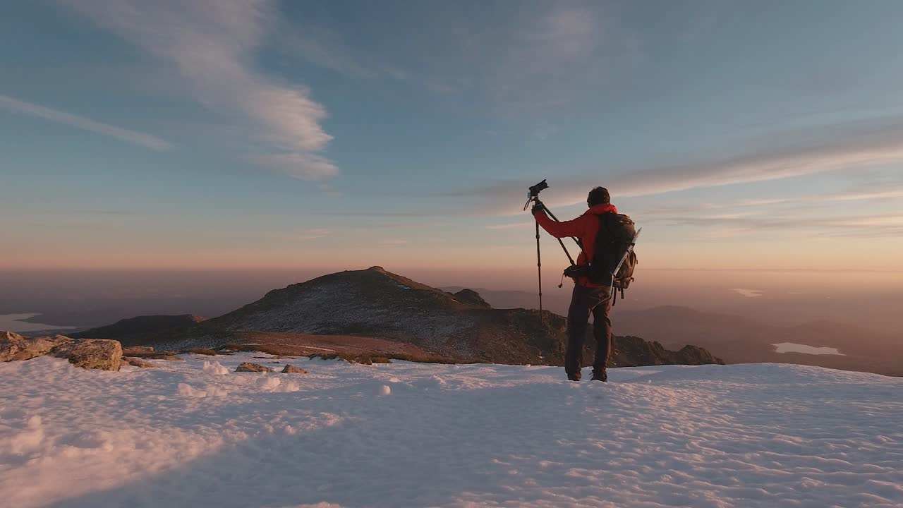 Ripresa grandangolare di spalle di un giovane escursionista che scatta foto con la sua macchina fotografica e treppiede sulla cima di una montagna innevata nei monti di Guadarrama, Madrid, Spagna.