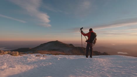 back view wide angle shot of young hiker taking photos with his camera and trípod on summit of snowy mountain in guadarrama mountains, madrid, spain