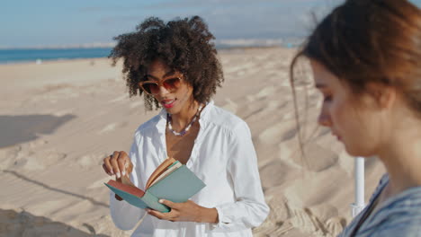 focused girl reading book at ocean picnic. two friends resting on sandy beach