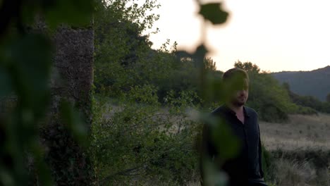 Man-in-a-black-shirt-walking-through-a-grass-field-during-sunset