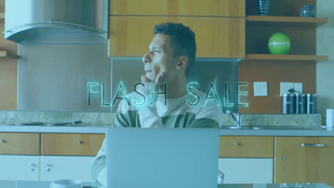 man working on laptop in kitchen with flash sale animation over him