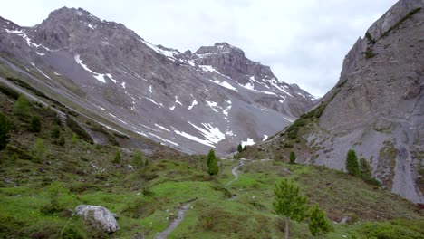 imágenes aéreas de drones que recorren un paisaje montañoso glacial con parches de nieve, árboles aislados, una ruta de senderismo alpina remota en suiza