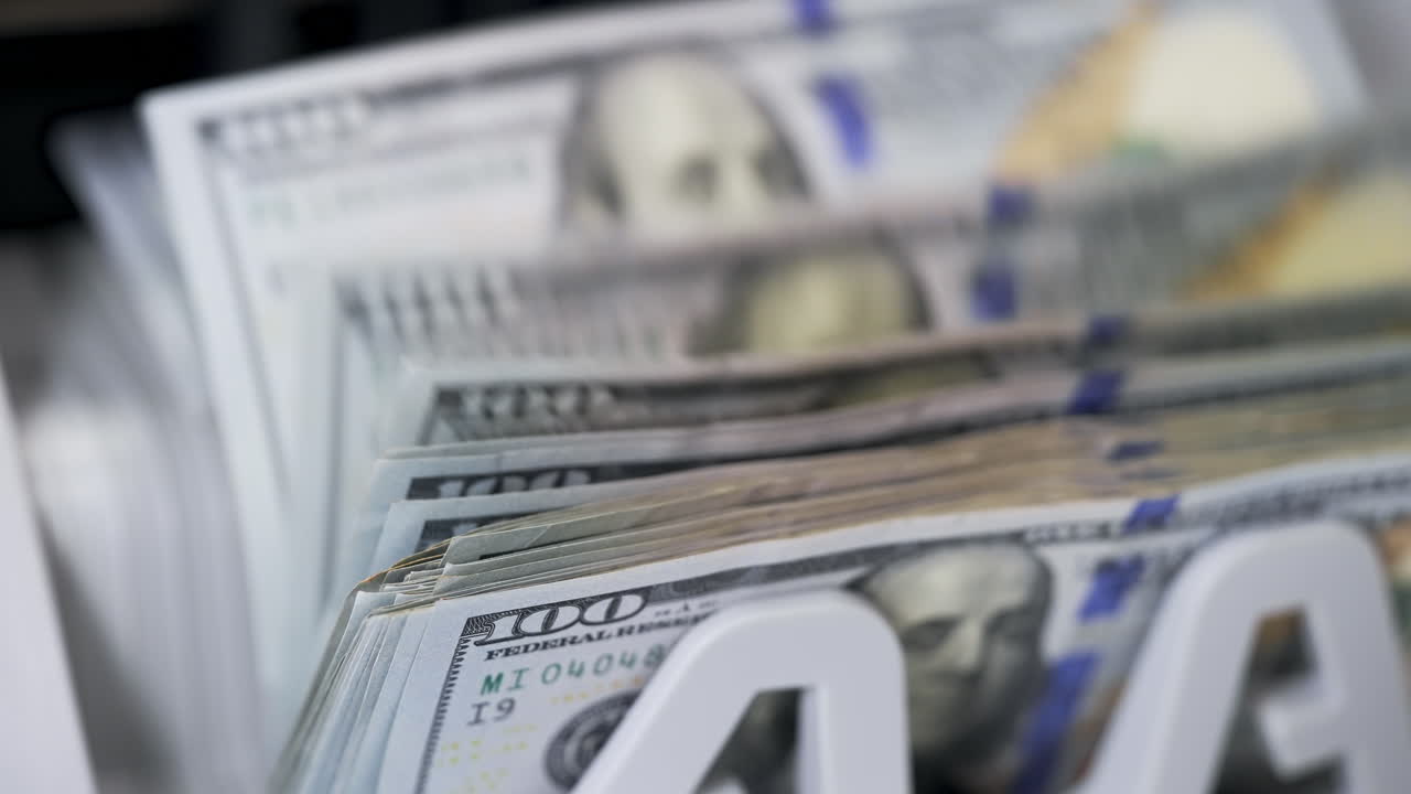 Money counting equipment for paper money calculation. Automatic mechanism for bank financial operations. Female hand taking a bundle of counted dollar bills from counting machine. Close-up.