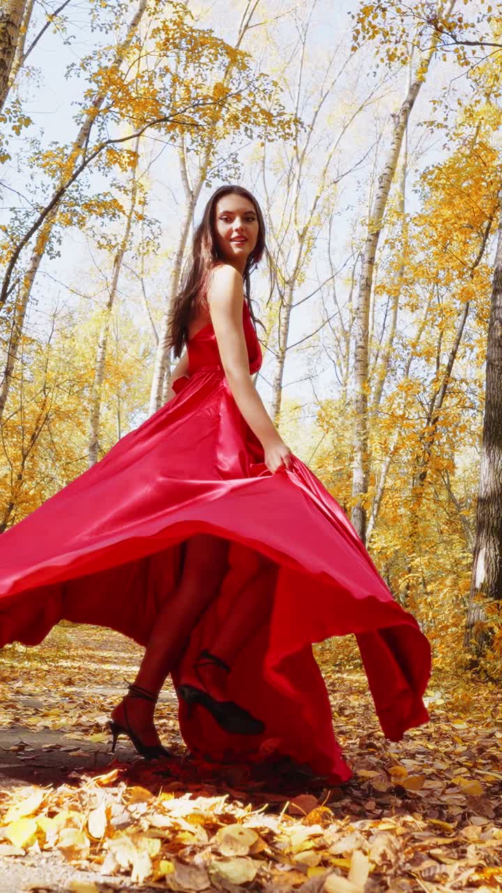 A Captivating Journey Through Autumn: A Woman in a Flowing Red Dress Graces the Golden Forest with Elegance and Style, Embracing the Seasonal Beauty