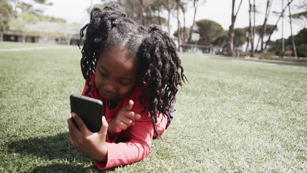 Young girl lying on grass using smartphone, enjoying outdoor playtime