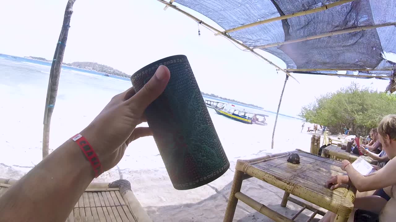 Man holding a cylindrical tube and looking through it towards the sea and tropical sandy beach with boats