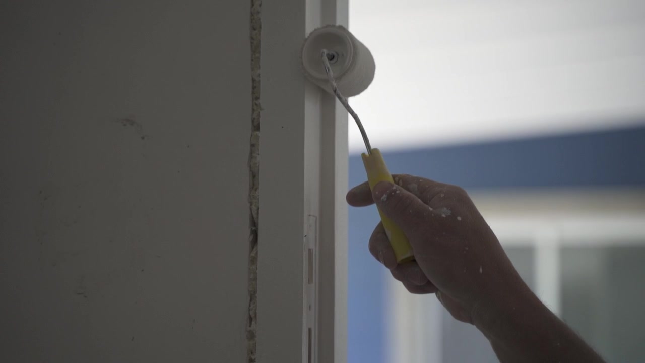 Close-up of a man's hand painting a door frame with a small paint roller.