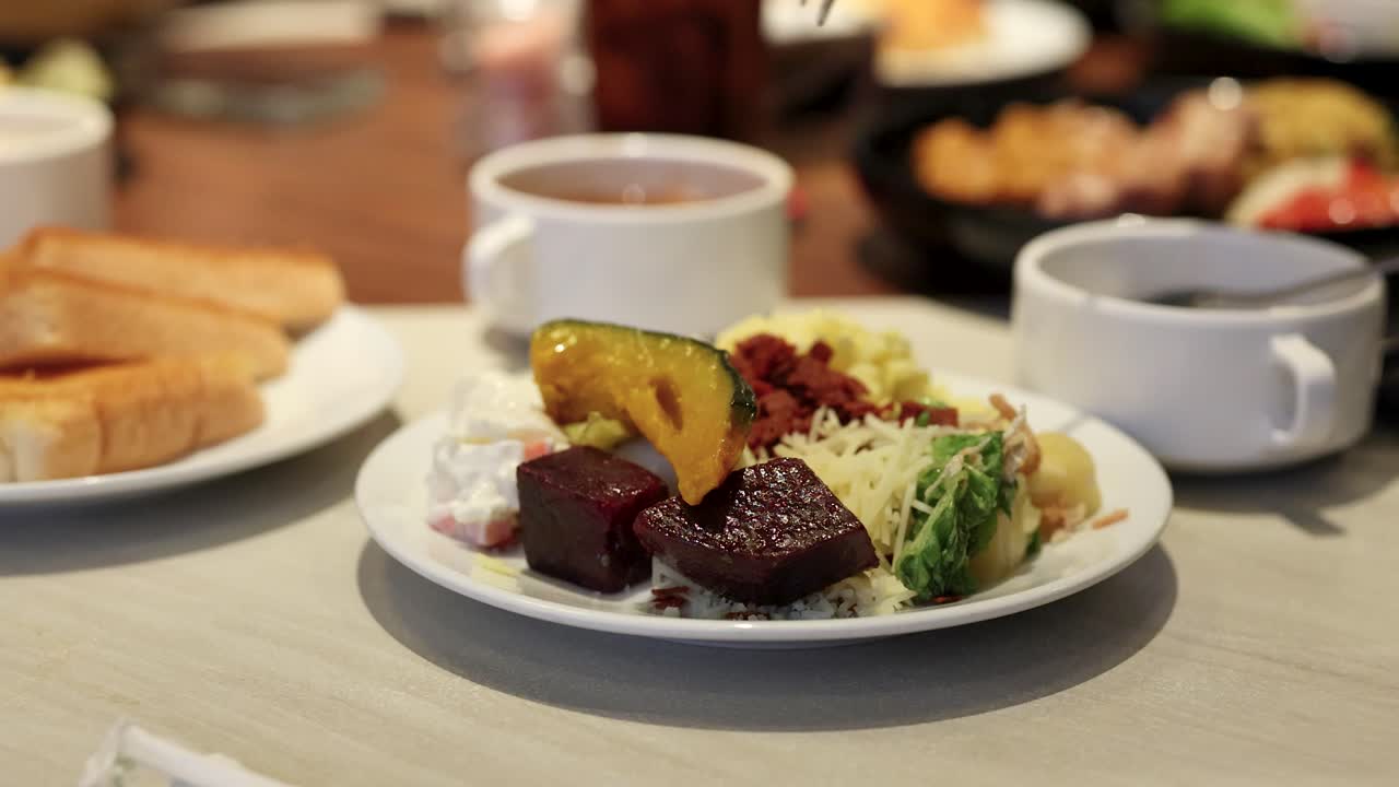 Hand uses fork to pick up roasted beetroot from colorful salad under warm lighting