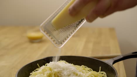 cheese being grated onto a saucepan of pasta