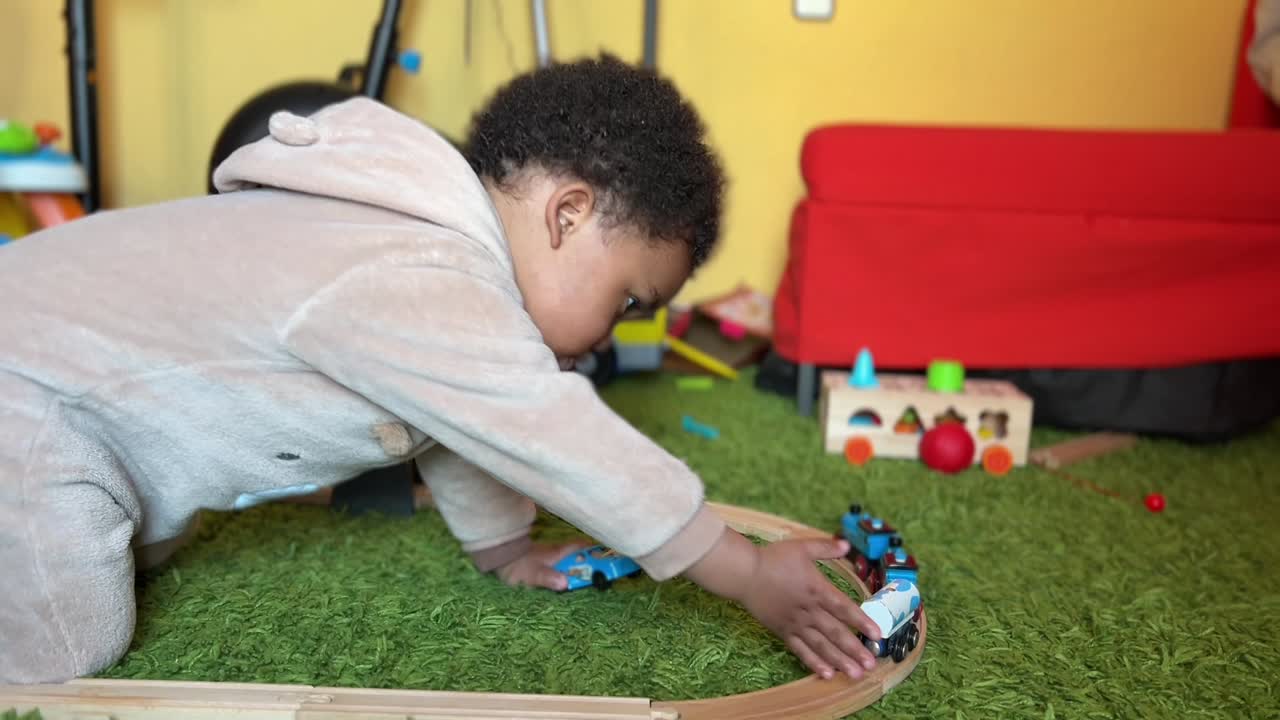 Two year old afroeuropean child playing at home with his toy train