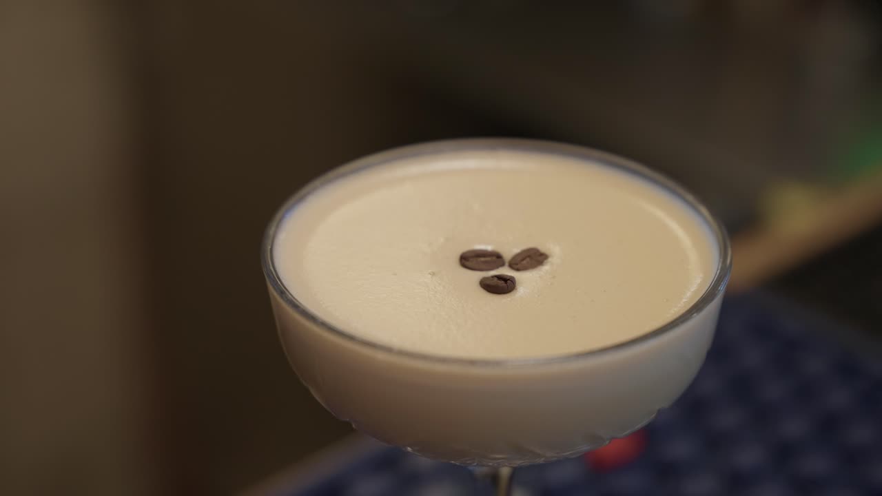 Mano che sistema chicchi di caffè su un cocktail spumoso in un bicchiere coppetta, primo piano