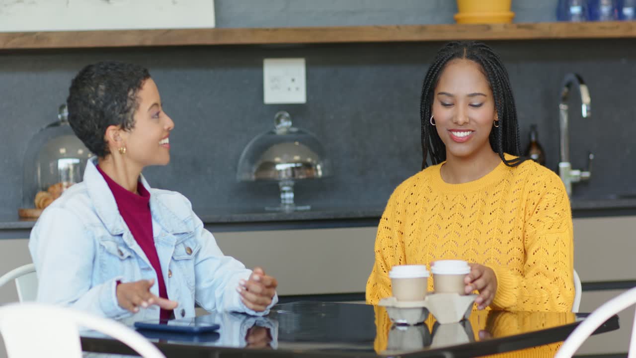 Diverse female friends picking up coffee cups and chatting at cafe after barista placing tray