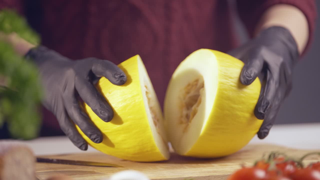 Slow-motion of a chef splitting a ripe yellow melon in half. Black gloves ensure hygiene, while the juicy texture is revealed. A wooden board and fresh ingredients create a vibrant kitchen scene