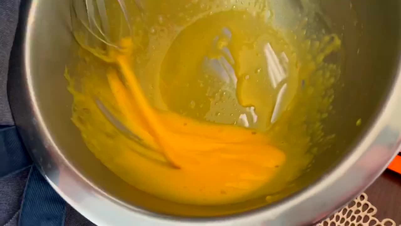 Hand manually whisking egg yolk in a large stainless steel bowl
