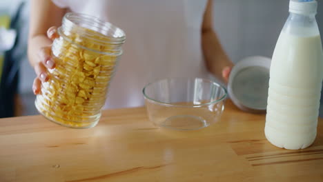 Frau-öffnet-Das-Glas-Und-Gießt-Cornflakes-In-Eine-Glasschüssel