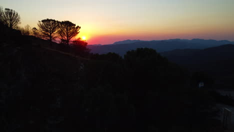 a drone pushes through the silhouetted trees and mountains at sunset