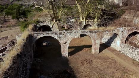 aerial: ex hacienda de san jacinto ixtoluca, aqueducts with rocky wall during the day in la mezquitera, morelos, mexico, crane down drone shot