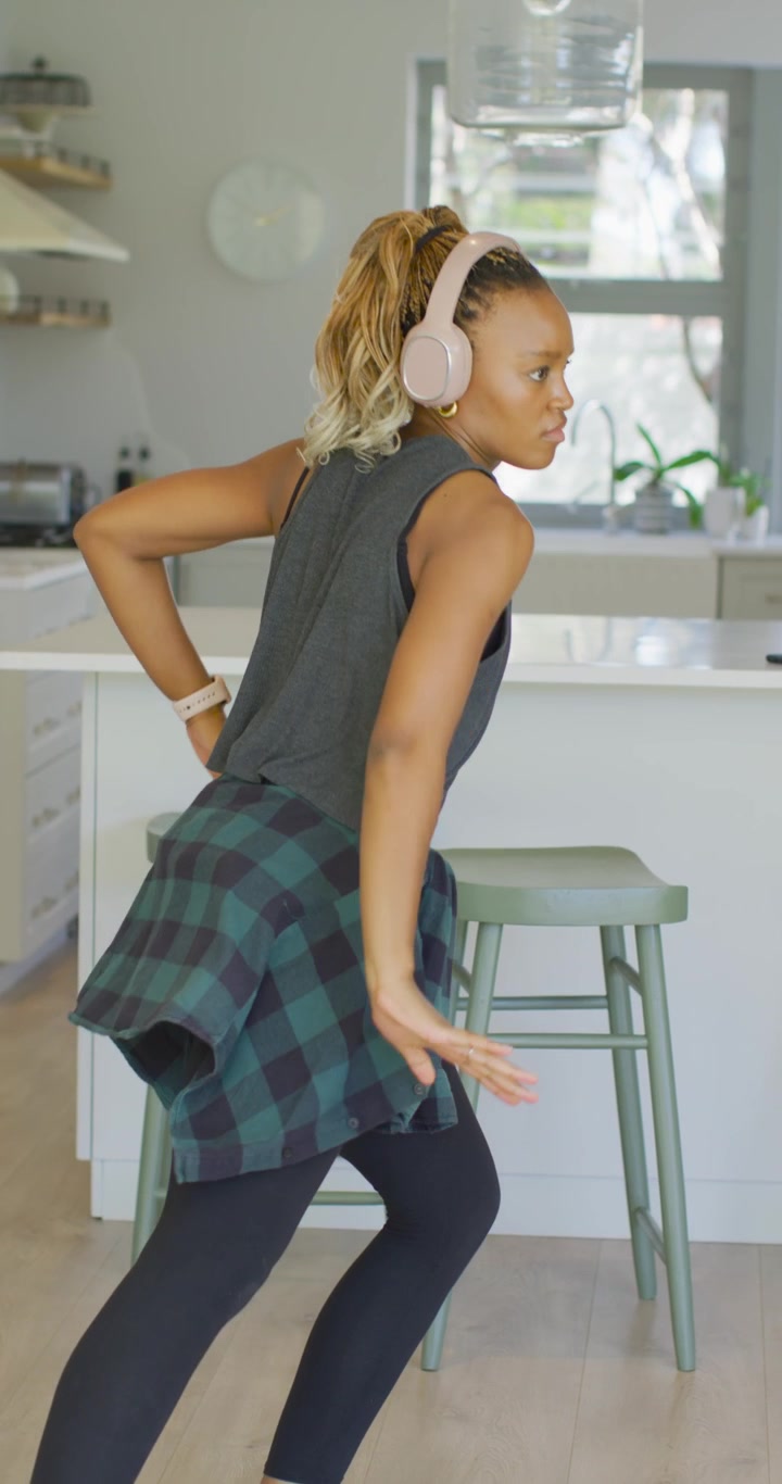 Vertical video: African American woman checking watch, punching twisting at kitchen island to music