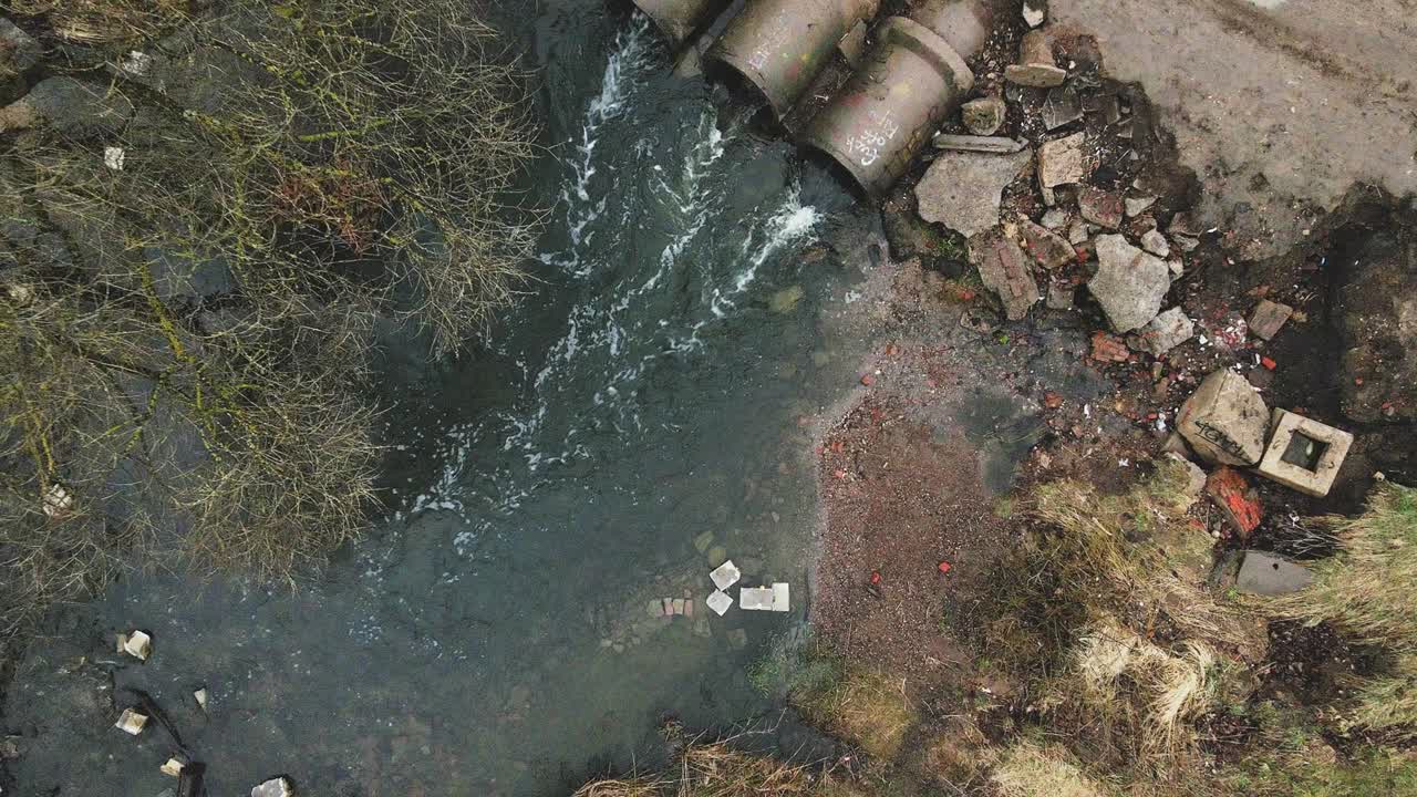 volando sobre alcantarillas de hormigón. corrientes de agua fluyen a través de tuberías de hormigó. cuerpo de agua contaminado en el parque. la cámara se baja.