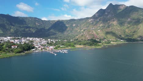 vista de avión no tripulado en guatemala volando sobre un lago azul rodeado de montañas verdes y volcanes en un día soleado en aitlan