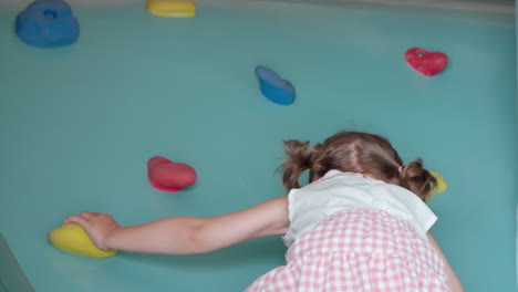 a girl toddler climbs up an indoor rock wall - slow-motion tracking