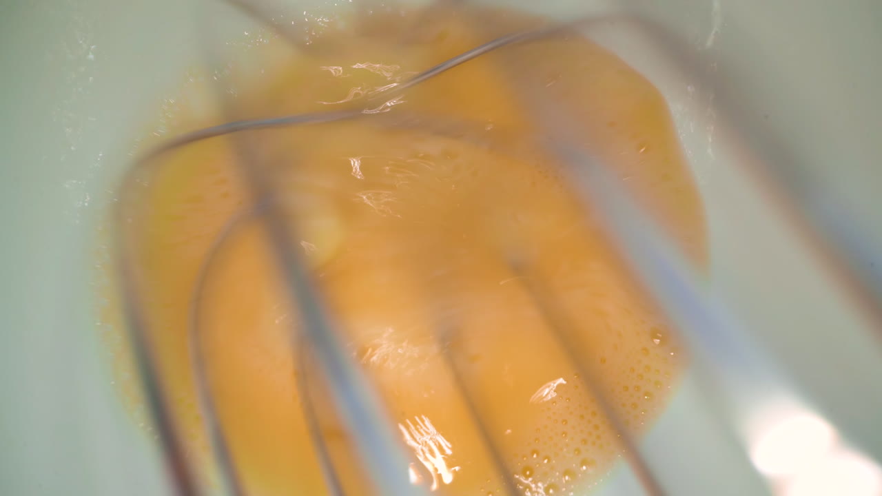 usando batidor para revueltas de huevo de pollo en tazón de cerámica blanca