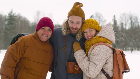 vista frontal de tres amigos en ropa de invierno sonriendo a la cámara en el bosque de invierno 1