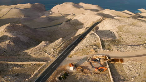 Vista-Aérea-De-Un-Coche-Conduciendo-Por-La-Carretera-Hacia-El-Mar-En-La-Isla-De-Pag-En-Croacia