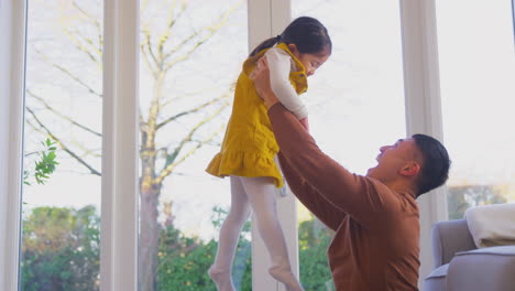 family having fun at home with dad lifting daughter into the air