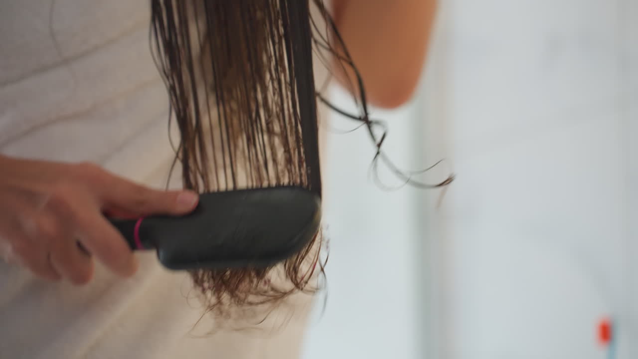 Caucasian woman wet hair hotel bathroom brushing and detangling long strands with paddle brush, wearing towel and silver bracelet, soft natural light, minimal luxury suite vibe, calm morning routine
