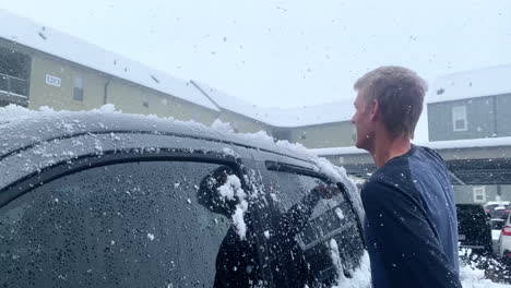 man taking snow off of car during a snowy day in 4k