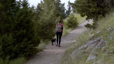 woman walking a small black dog on a hiking trail