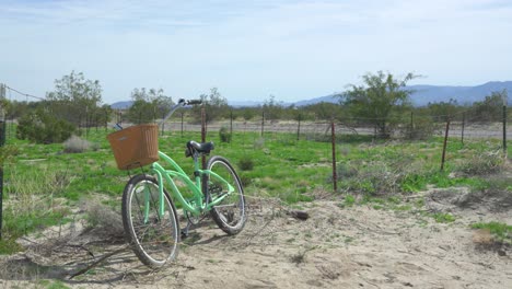 Weite-Aufnahme-Eines-Strandfahrrads-Mit-Korb,-Das-In-Der-Anza-Borrego-Wüste-Zurückgelassen-Wurde-Und-An-Einem-Rostigen-Zaun-Lehnt