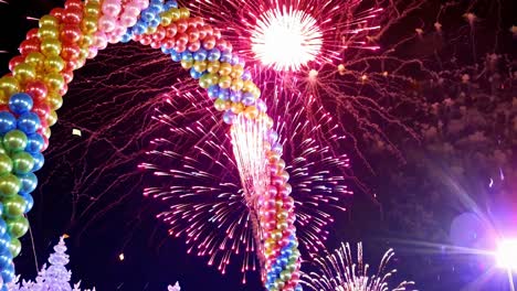colorful confetti falling from the sky during night celebration with balloons arch and fireworks exploding in the background, creating a vibrant and festive atmosphere
