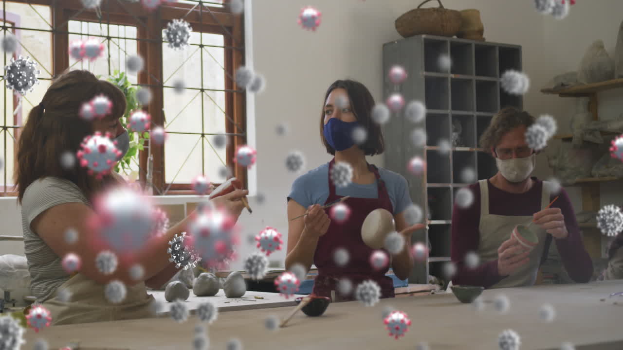 코로나 19 세포의 애니메이션은 얼굴 마스크를 착용하여 도자기 스튜디오에서 일하는 남자와 여자 위에 있습니다.