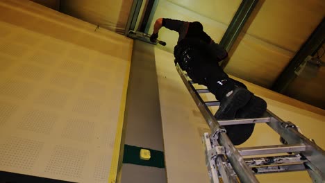 low-lit interior scene as craftsman paints industrial post from steep height