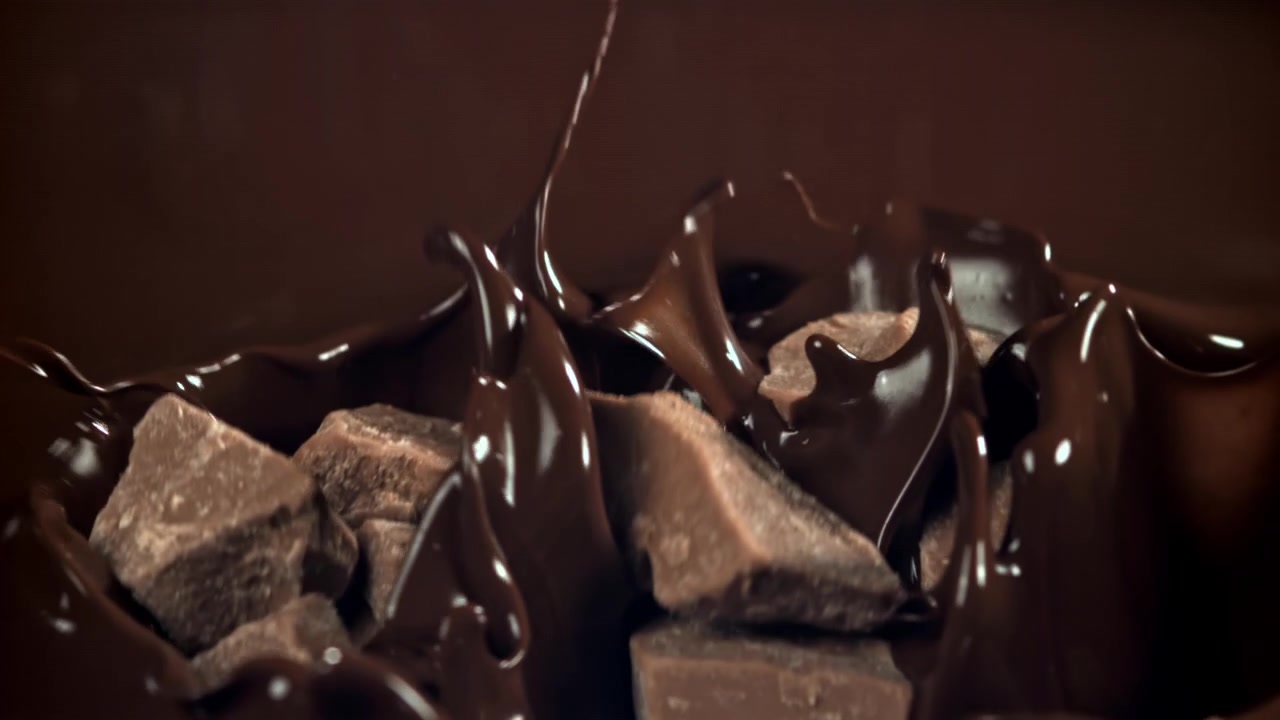 Pezzi di cioccolato che si tuffano al rallentatore nel cioccolato fuso