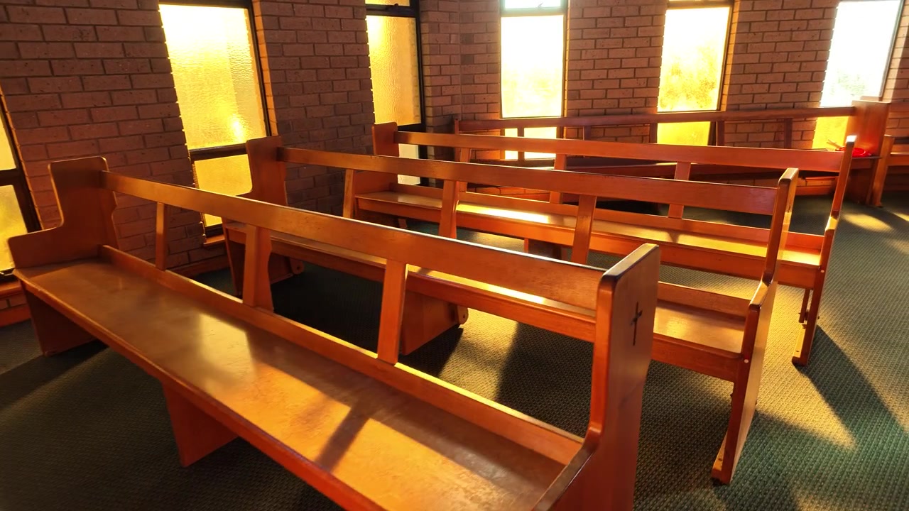 Calda luce solare proietta lunghe ombre sui banchi di legno vuoti all'interno di una chiesa tranquilla. La luce dorata illumina l'interno sereno e pacifico.