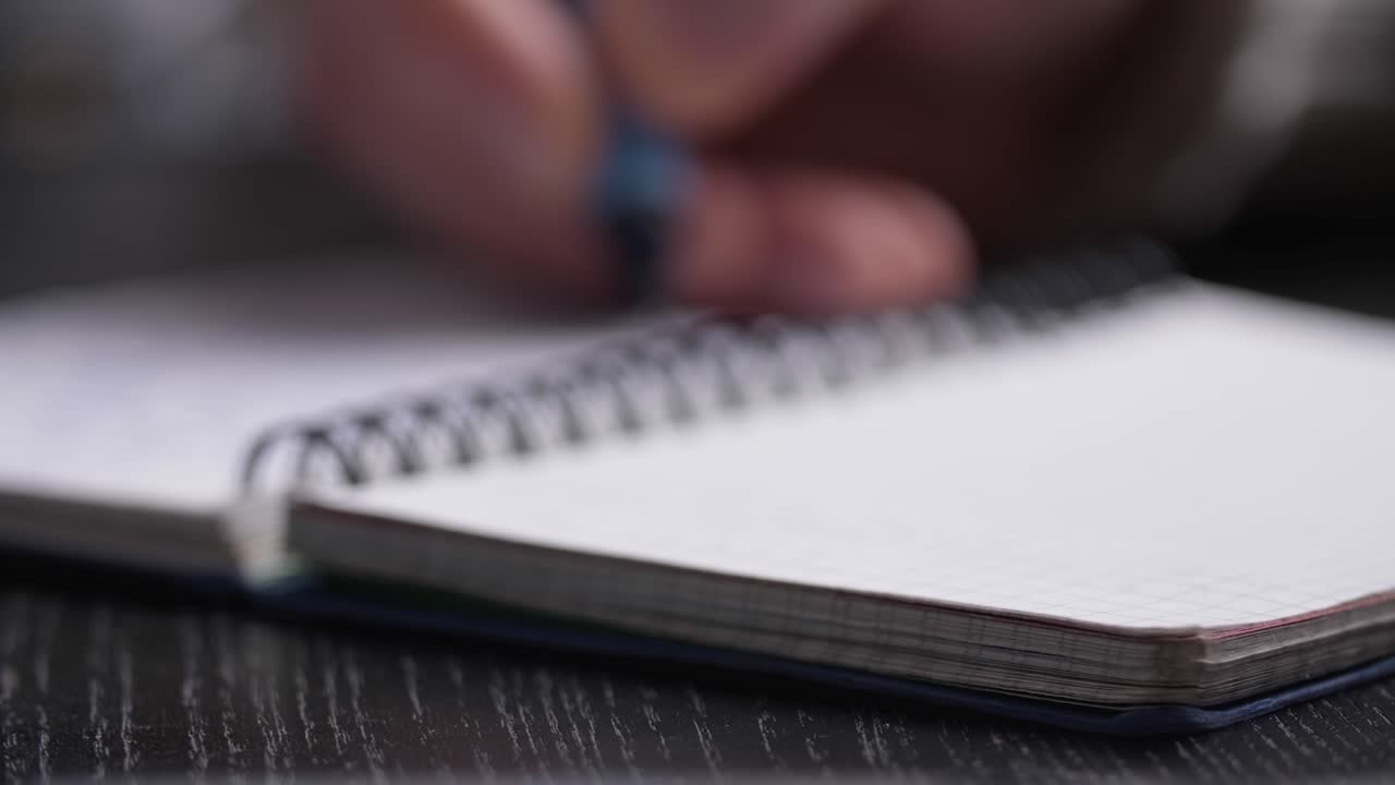 Close up of man's hands writing in spiral notepad placed on wooden black desktop